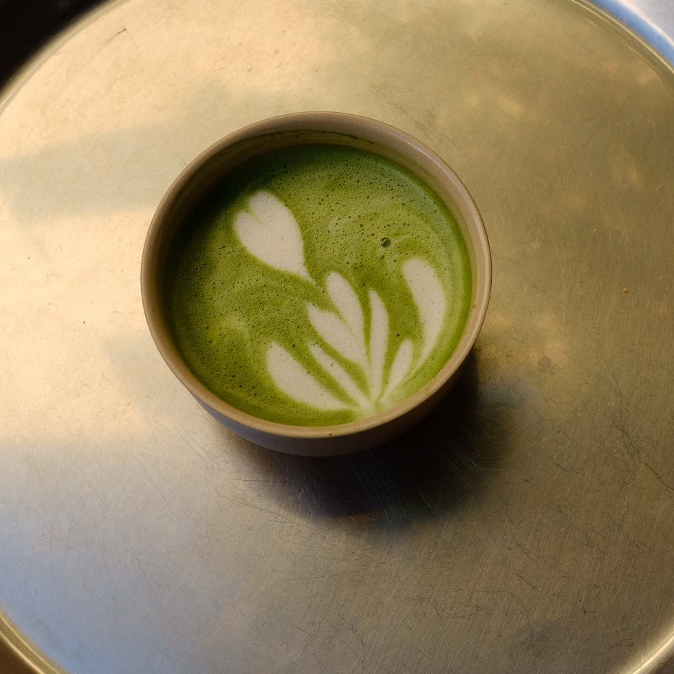 Cup of green matcha latte with leaf design on a metallic tray
